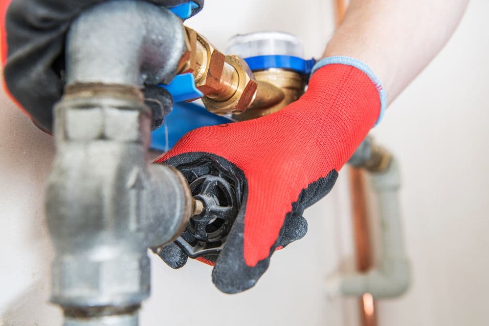 Person in red gloves adjusting a water meter valve on copper plumbing.